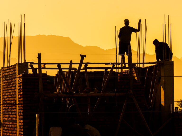 OUR STORY Silhouette of construction workers on a building site at sunset, showcasing urban development.